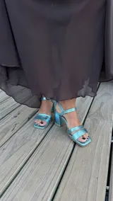 Sandalia de tacón cuadrado medio, con diseño de tiras horizontales y punta cuadrada. Presenta un acabado metalizado en color turquesa y cierre con pulsera al tobillo.
