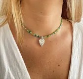 Gargantilla de cuentas de vidrio facetado en tonos verde y amarillo, con dije de hoja plateada.