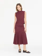 Pollera de tejido punto color bordó, ajustada hasta la cadera con caída acampanada en la parte inferior. Presenta detalles de hotfix en el frente.