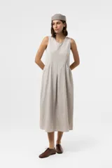 Vestido midi sin mangas de color beige, con silueta amplia y caída relajada, escote redondo y recortes frontales con volumen.