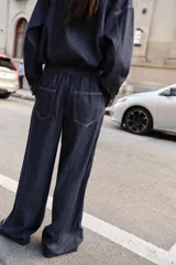 Jeans de tiro alto color azul oscuro, con cintura elástica en la espalda, bolsillos delanteros y bolsillos de plastrón en la espalda. Presenta pernera ancha y cierre frontal con cremallera y botón a presión.