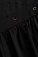 Pollera corta negra con cintura en V decorada con ojales metálicos. Presenta pliegues en la parte superior y un frunce que da volumen a la falda.