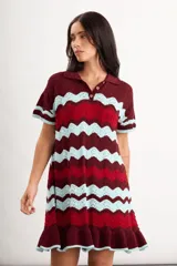 Vestido corto de punto con patrón en zigzag de franjas azules, marrones y amarillas, cuello polo con cierre frontal de un botón, mangas cortas y volado en el ruedo.