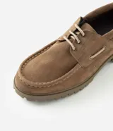 Zapato estilo náutico para hombre, confeccionado en cuero gamuza color marrón. Presenta diseño liso con puntera redondeada, costura aparente en la capellada, cordones bicolor y suela tractorada engomada.