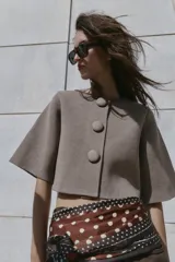 Chaqueta corta de punto color beige, con cuello redondo y manga tres cuartos. Cierre frontal con tres botones forrados a tono.