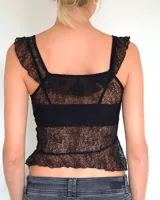 Top de encaje negro con breteles anchos y diseño asimétrico en el ruedo. Presenta un estilo romántico con volados sutiles en los bordes y una estructura que simula un corset.