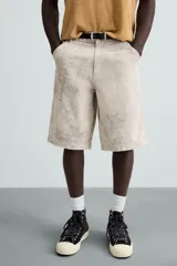 Bermuda de algodón color beige claro con efecto lavado y estampado abstracto en tonos grises. Diseño de corte relajado con cierre frontal de botón y cremallera, bolsillos delanteros y bolsillos traseros de plastrón.