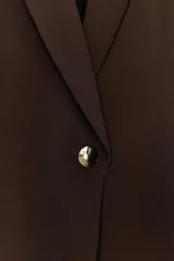 Blazer negro con cuello solapa con muescas, hombreras y forro interior a tono. Presenta manga por debajo del codo con detalle de drapeado y falsos bolsillos de vivo en el delantero, con cierre frontal de un solo botón dorado.
