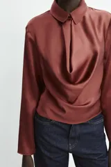 Blusa de tejido satinado con cuello solapa, manga larga y detalle de abertura drapeada en el pecho. Cierre frontal con botón forrado.