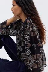 Blusa negra con estampado paisley en tonos naranja, azul y blanco. Diseño oversized con mangas largas amplias, canesú con costura fruncida y abertura con tiras para atar en la espalda.