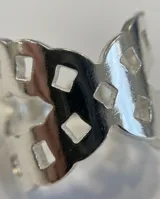 Anillo ancho de acero plateado con diseño calado de perforaciones geométricas.