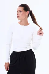 Remera de manga larga en tejido de punto acanalado, color blanco, con cuello redondo y cierre frontal parcial con botones.