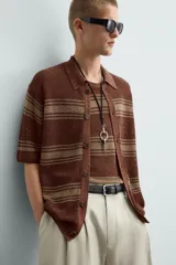 Camisa de punto de manga corta, color marrón rojizo con rayas horizontales en tono beige/verde oliva. Presenta cuello solapa y cierre frontal de botones.