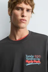 Camiseta negra con efecto lavado, corte boxy fit, cuello redondo y manga corta. Presenta un estampado frontal con texto en tonos turquesa, rojo y blanco que dice "Tuesday 600 Marathon Day Hyde Park".