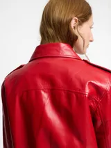 Chaqueta biker negra de cuero sintético con tachas plateadas en los hombros y solapas, cierre asimétrico con cremallera, cinturón ajustable con hebilla y detalles metálicos.