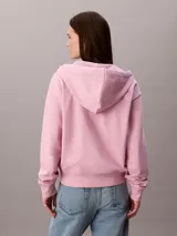 Buzo con capucha de Calvin Klein, de corte cropped y color rosado, confeccionado en mezcla de algodón y poliéster. Cuenta con cierre frontal de cremallera, cordones ajustables en la capucha y bolsillos tipo canguro. Presenta el logo de la marca bordado discretamente en el pecho.