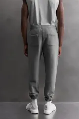 Pantalón jogger gris de corte regular fit, confeccionado en tejido de algodón con interior afelpado. Cuenta con cintura elástica ajustable con cordón, bolsillos laterales de vivo y traseros de plastrón. Presenta un texto estampado en color bordó en la pernera y bajo acabado en puño con elástico. Incluye un parche con logo combinado a contraste en la cintura.