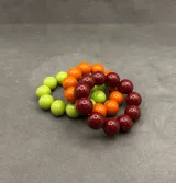 Pulsera elástica compuesta por cuentas esféricas de resina en tonos verde lima, naranja y bordó.