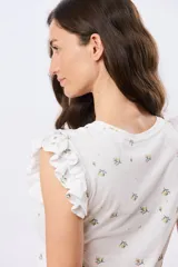 Remera blanca de algodón con estampado de ramas y pequeños frutos, escote redondo y mangas cortas con volados.