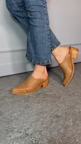 Zueco de cuero color camel, con punta fina cerrada, diseño perforado en los laterales y tacón ancho de madera.