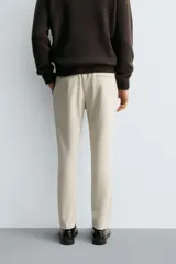 Pantalón de corte slim fit confeccionado en tejido elástico, con cintura elástica, cierre frontal con cremallera y botón, bolsillos laterales y bolsillos traseros de vivo.