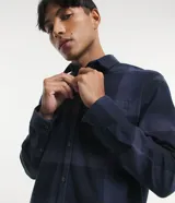 Camisa de manga larga con diseño de cuadros en tonos marrones, confeccionada en algodón. Presenta cuello camisero, cierre frontal con botones y un bolsillo en el pecho con botón.