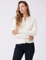 Cardigan blanco de punto aran con cuello redondo y cierre frontal de botones dorados. Presenta bolsillos simulados en la parte delantera.