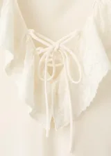 Vestido midi recto color beige sin mangas, con cuello en V con solapa de volantes bordados y cordones entrecruzados en el escote.