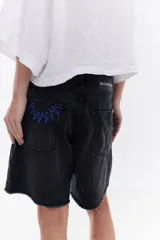 Bermuda de denim negro tipo jeans, con tiro medio, bolsillos traseros con bordado en contraste y ruedo desflecado.
