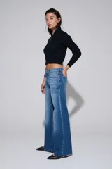 Pantalón de jean de tiro medio y pierna ancha, con lavado claro y zonas desgastadas.