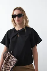 Top negro de manga corta con detalle de nudo en el escote y abertura tipo gota. Presenta una silueta relajada y textura sutil en la tela.