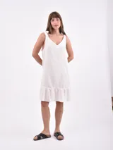 Vestido corto blanco de corte holgado, con escote en V y detalle de lazos para anudar en los tirantes. Cuenta con un volante fruncido en el ruedo.