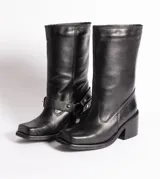 Bota de cuero negra con caña media, punta cuadrada, taco bloque y arnés con hebillas y tachas plateadas.