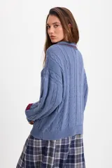 Sweater de punto trenzado color azul, con cuello polo, cierre frontal de tres botones y detalle de etiqueta roja en el puño.