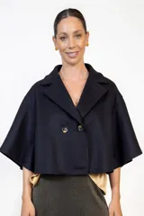 Capa de paño color negro con diseño de doble botonadura frontal y solapas clásicas. Presenta un corte holgado y mangas amplias tipo capa, confeccionada en tejido de poliéster.