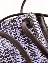 Bandolera pequeña confeccionada en cuero vacuno negro con paneles frontales y posteriores de rafia tejida en tonos negros y rosados. Posee cierre superior con cordón ajustable y broche snap metálico, asas largas para el hombro e interior forrado en algodón.
