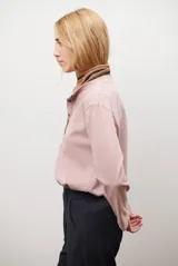 Remera de manga larga en color rosado, con cuello redondo y cierre frontal parcial con botones. Presenta un diseño de corte recto y estilo minimalista.