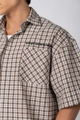 Camisa de manga corta de popelina con patrón a cuadros, calce boxy y largo a la cintura, con bolsillos y canesú cortados en diagonal.