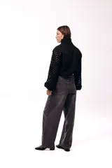 Campera de jean negra con mangas largas tejidas en crochet con diseño calado y detalles florales en relieve. Presenta cuello camisero, cierre frontal y bolsillos en el pecho.