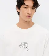 Remera de corte relajado color blanco, con cuello redondo y manga corta. Presenta un estampado pequeño en el centro del pecho con la inscripción 'Most Wanted' y el diseño de los Hermanos Metralla.