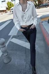 Camisa corta de cuello solapa y manga larga, con trabillas decorativas en los hombros. Presenta pliegues delanteros, elástico en la espalda y cierre frontal con botones.