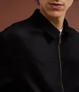 Campera masculina de estilo casual con cuello inglés, cierre frontal por cremallera, bolsillos laterales y ajuste elástico en el bajo. Presenta detalles de recortes en la parte superior delantera.