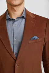 Blazer de pana color marrón oscuro, con cierre frontal de dos botones, solapas clásicas y bolsillos laterales con solapa. Presenta un diseño estructurado y elegante.