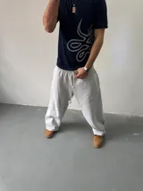 Pantalón de jogging gris melange de corte baggy, confeccionado en algodón. Presenta cintura elástica con cordón largo ajustable, bordado decorativo en la pierna izquierda y botones metálicos en la parte inferior de la botamanga para ajustar el ancho.