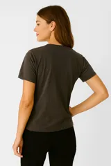 Remera de algodón color marrón con estampado de una figura femenina en blanco y negro, con detalles de lentejuelas en el vestido. Tiene cuello redondo y mangas cortas.