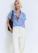Camisa celeste con rayas verticales blancas, de corte recto, cuello camisero y mangas cortas murciélago. Cierre frontal con dos botones.