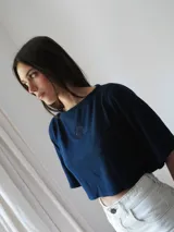 Top corto azul marino de punto, con mangas cortas amplias, cuello redondo y detalle de escudo bordado en la parte delantera.