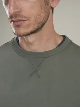 Sweater verde militar de cuello redondo y manga larga con detalle de bolsillo con solapa en la manga izquierda.