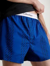 Conjunto de pijama Calvin Klein compuesto por una remera negra de algodón con cuello redondo y mangas cortas, y un short azul estampado con cintura elástica con el logo de la marca.