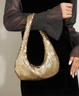 Bolso de mano tipo baguette, color negro, confeccionado en malla metálica con efecto lentejuelas o escamas. Tiene un asa única curva y cierre de cremallera en la parte superior.